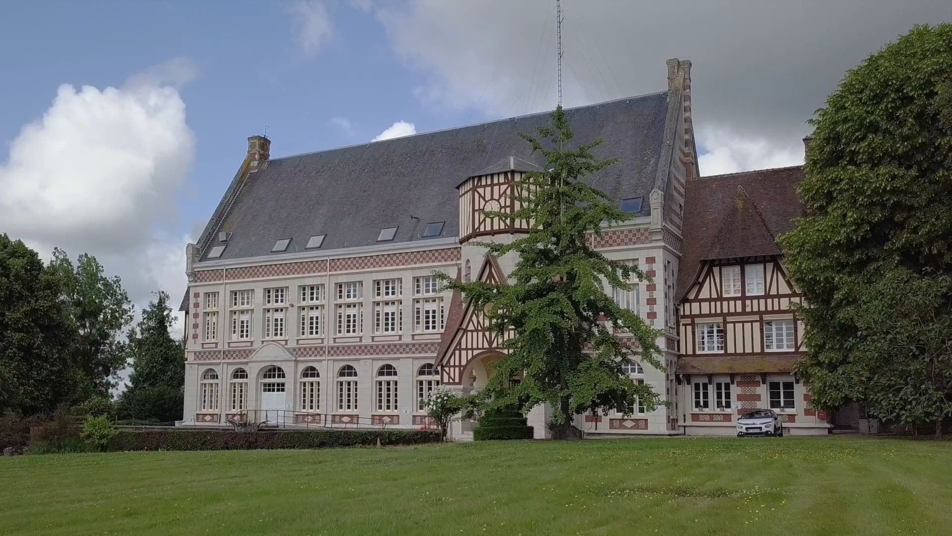 La façade de l’église et sa tour à colombages, au bout de la pelouse, sous les nuages.